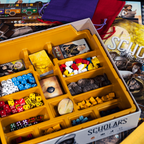 Board game components including dice and pieces in a yellow box with 'Scholars' branding.