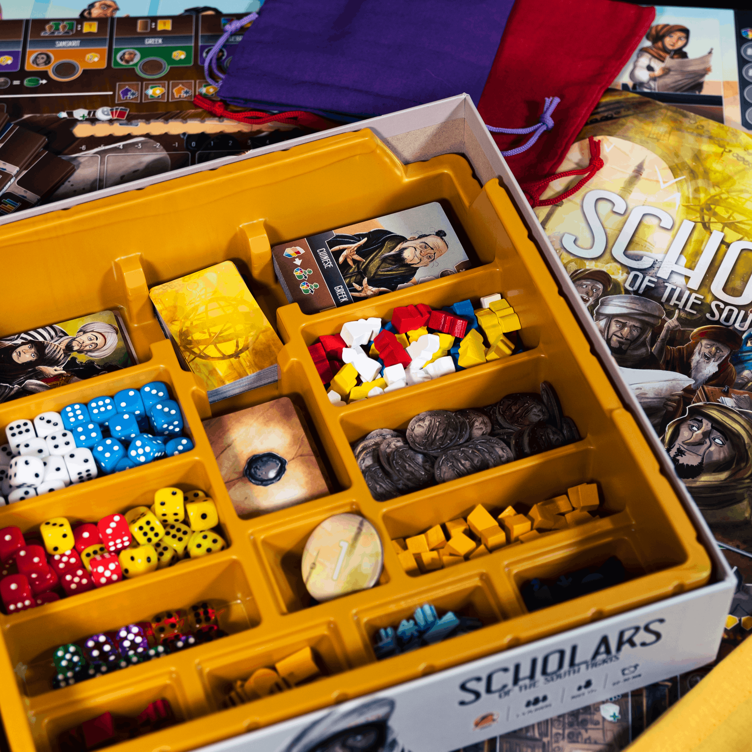Board game components including dice and pieces in a yellow box with 'Scholars' branding.