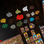 Board game components including cards, tokens, and a box on a dark surface