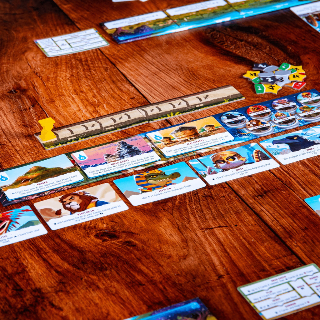 A close-up of a board game spread on a wooden tabletop, showing colorful illustrated cards, tokens, and game pieces arranged across the surface.