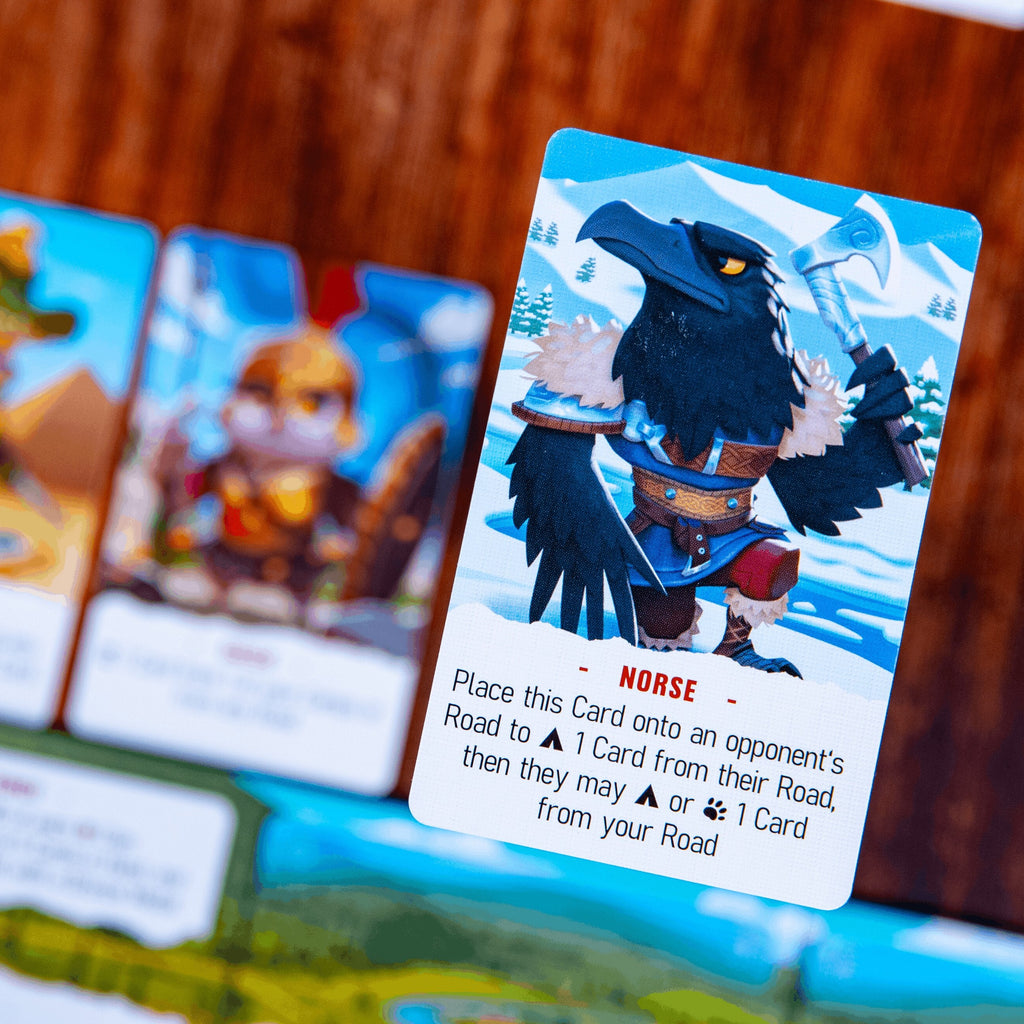 A close-up of a card game board with illustrated cards, including a prominent card featuring a black raven character labeled NORSE, set against a wooden surface.