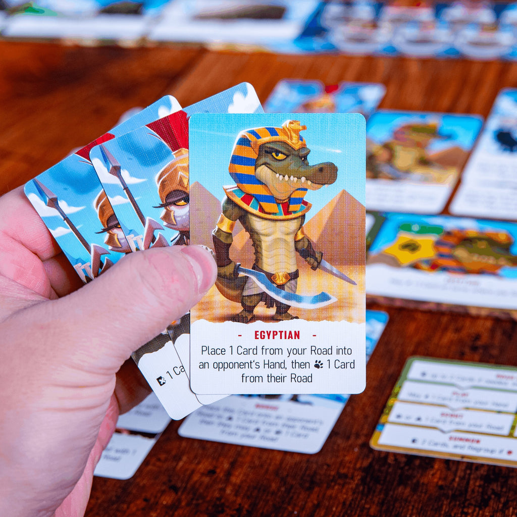 Hand holding a game card featuring an Egyptian-themed character with other game cards on a wooden table.
